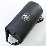 Load image into Gallery viewer, En person står på steiner ved vannet og holder en svart NEST-tørrbag med logo på.
